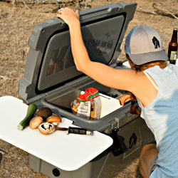 Women opening KONG Cooler with cutting board on the left of the cooler