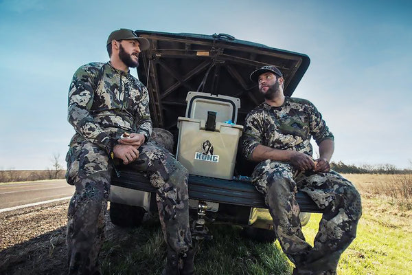 Two people sitting on tail gate of truck with KONG Cooler 20 quart open with ice inside