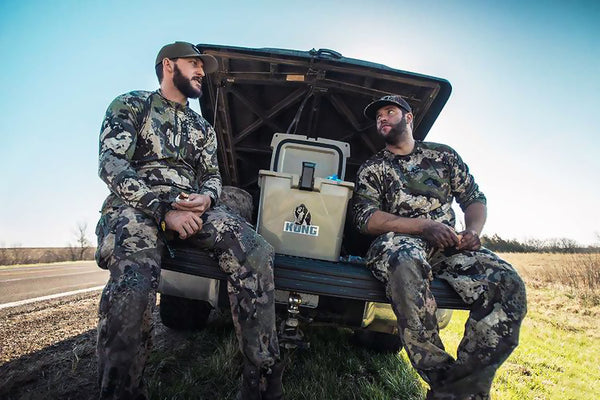 Two people sitting on tail gate of truck with KONG Cooler 20 quart open with ice inside